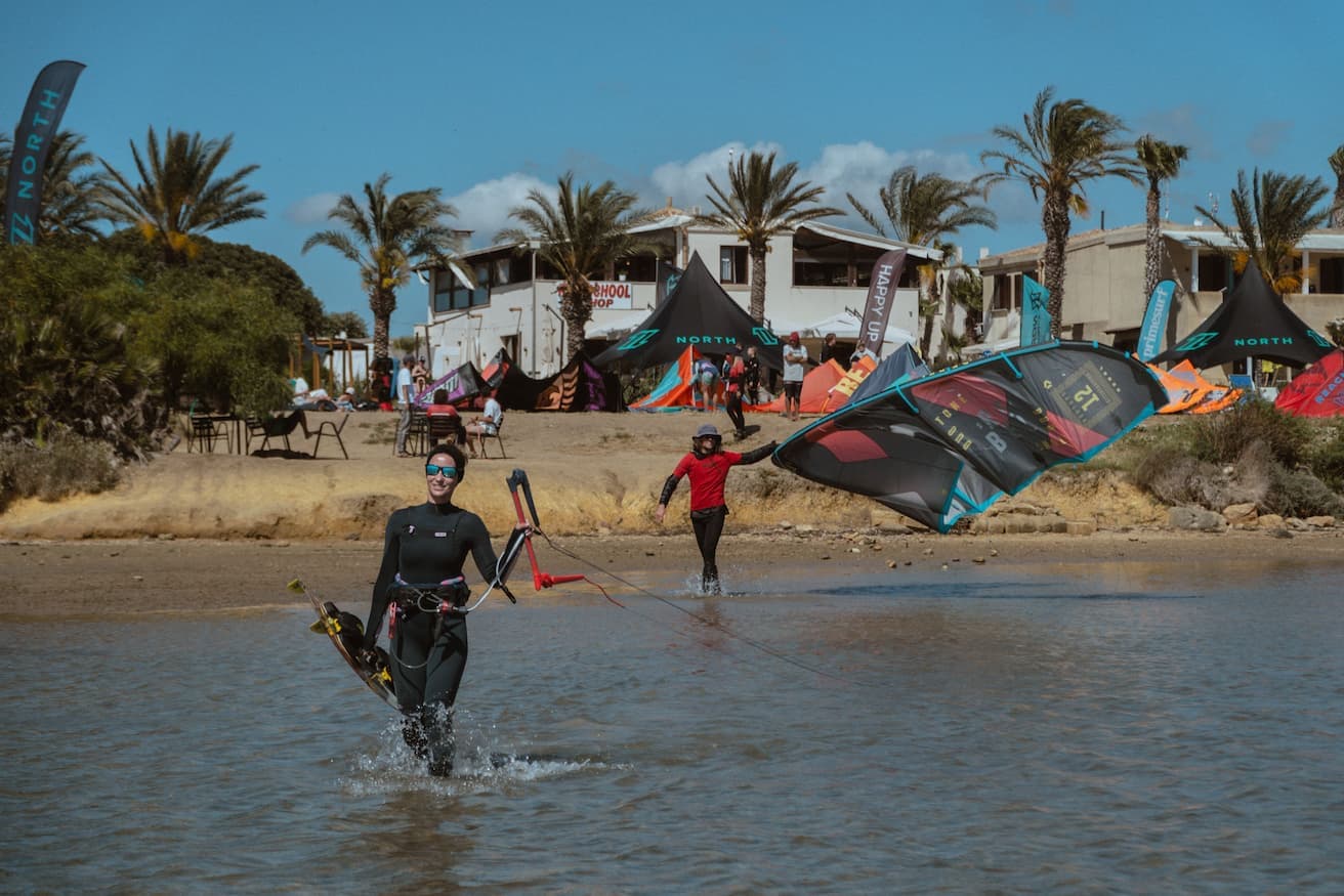 happy rental kiter walking in shallow water with a kite instructor following her with a kite in hand